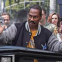 Eddie Murphy as Axel Foley stands by an overturned car with his hands raised in 'Beverly Hills Cop: Axel F.'