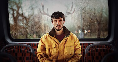 Richard Gadd as Donny Dunn sits in the back of a bus with reindeer antlers outside, behind his head in Season 1 of 'Baby Reindeer'