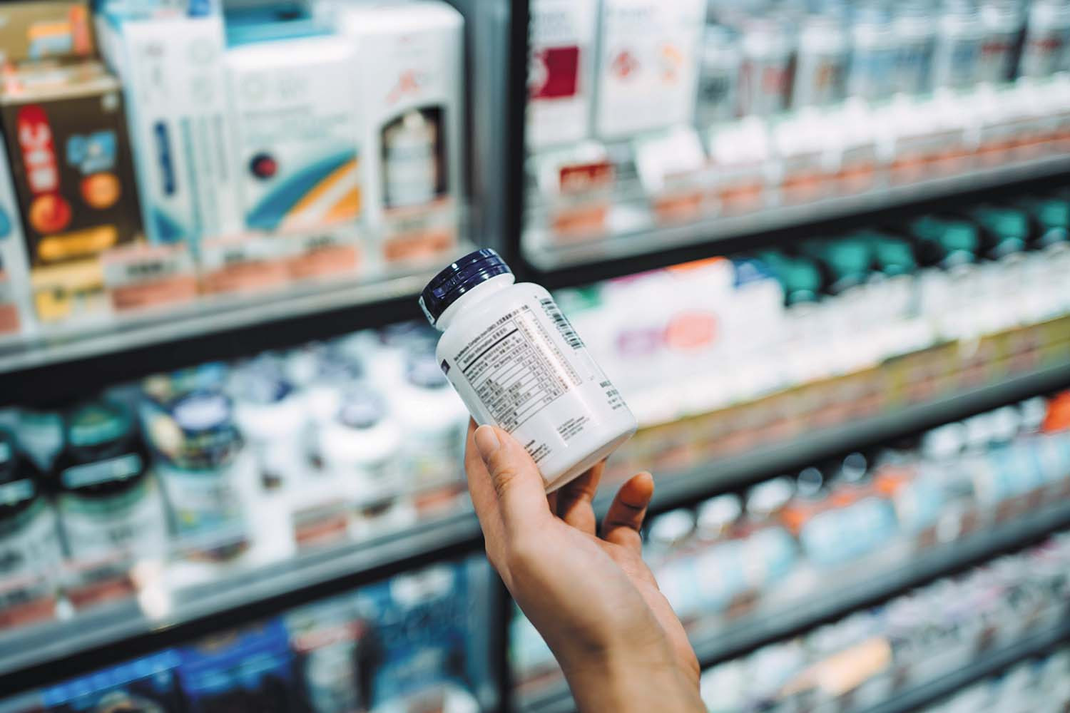 photo in a drugstore aisle of a hand holding a supplement bottle with the label facing the viewer