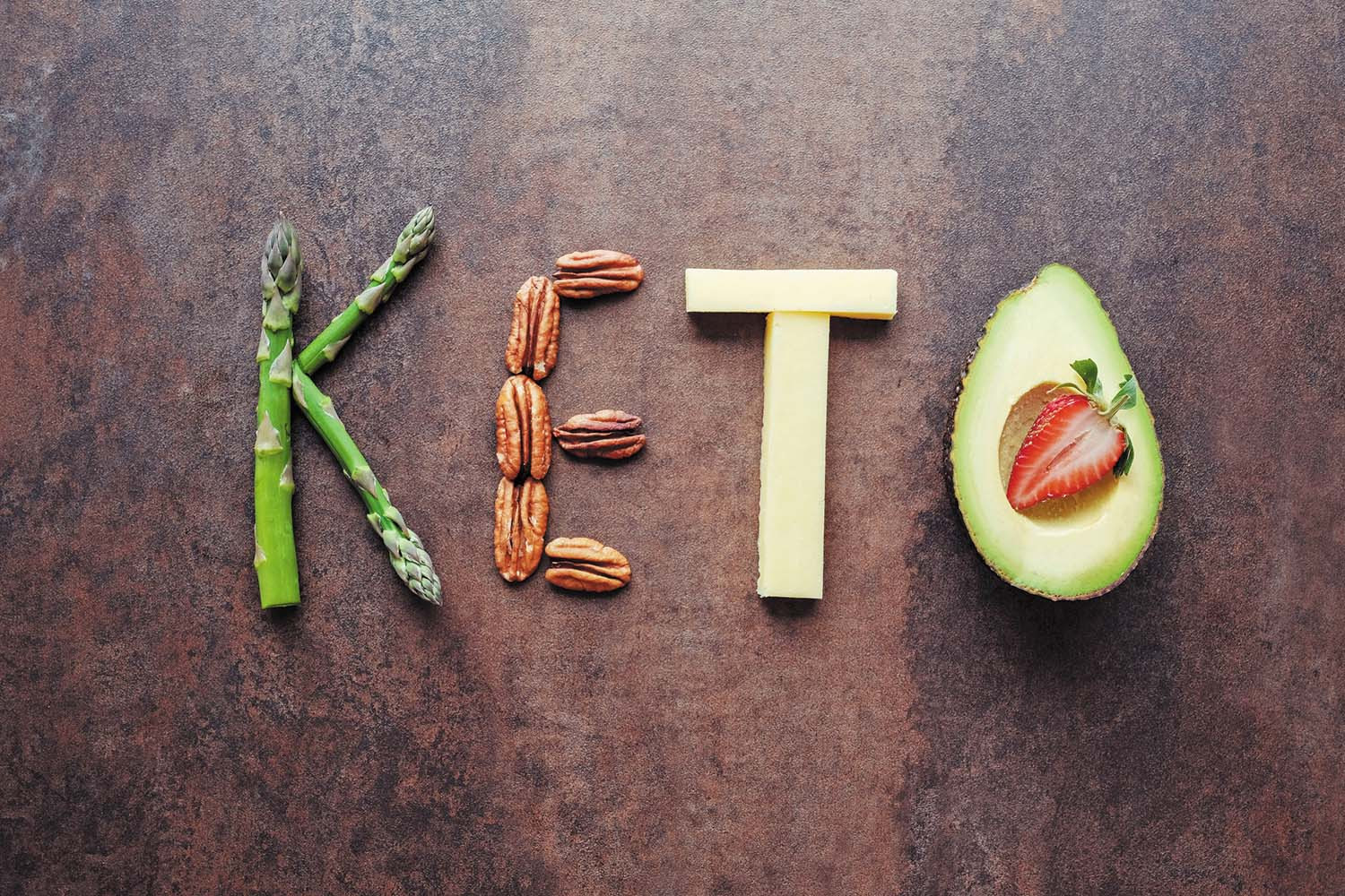 photo of foods (asparagus, pecans, cheese, and avocado) arranged on a wood board to spell out the word keto