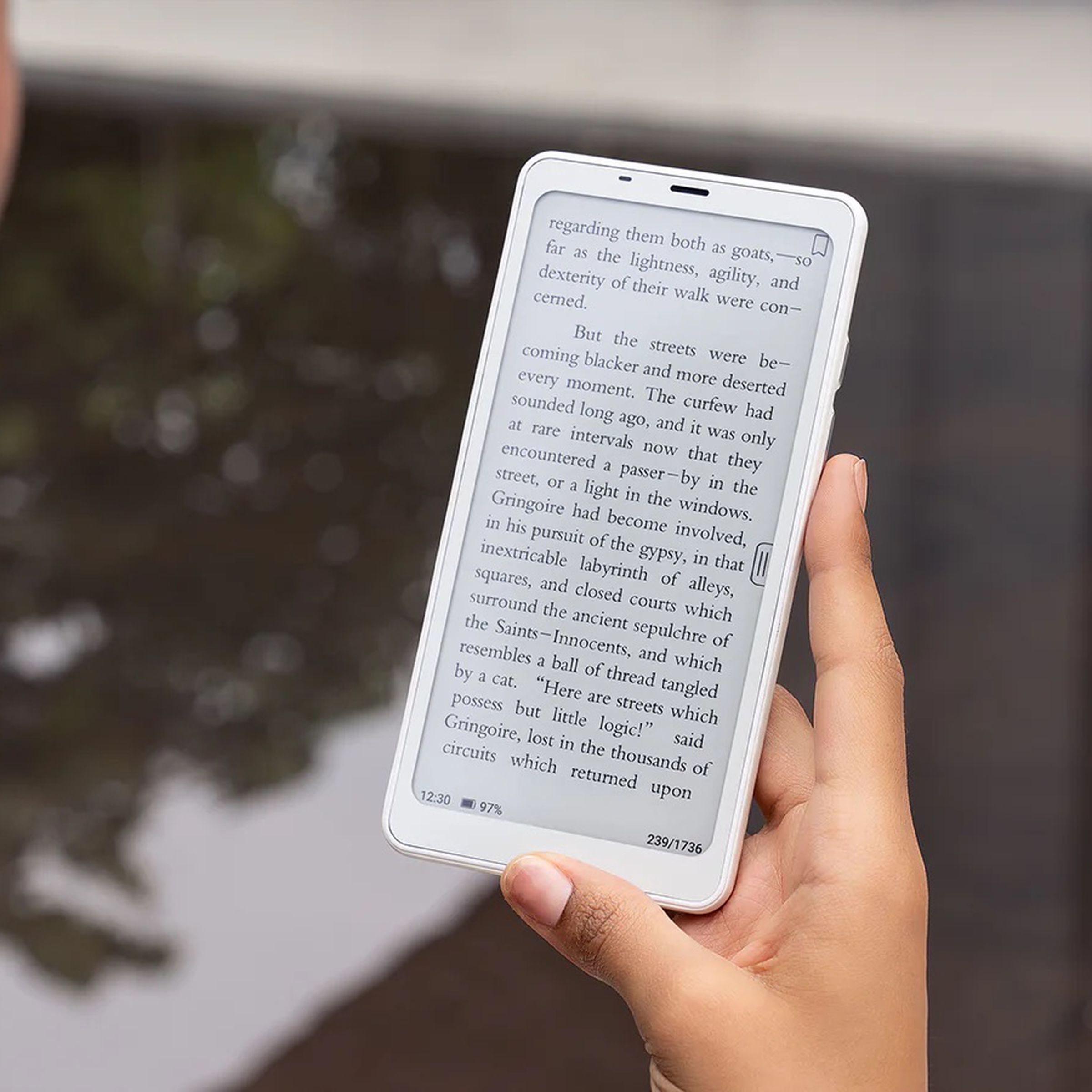 A photo of a person using a smartphone-like device near water.