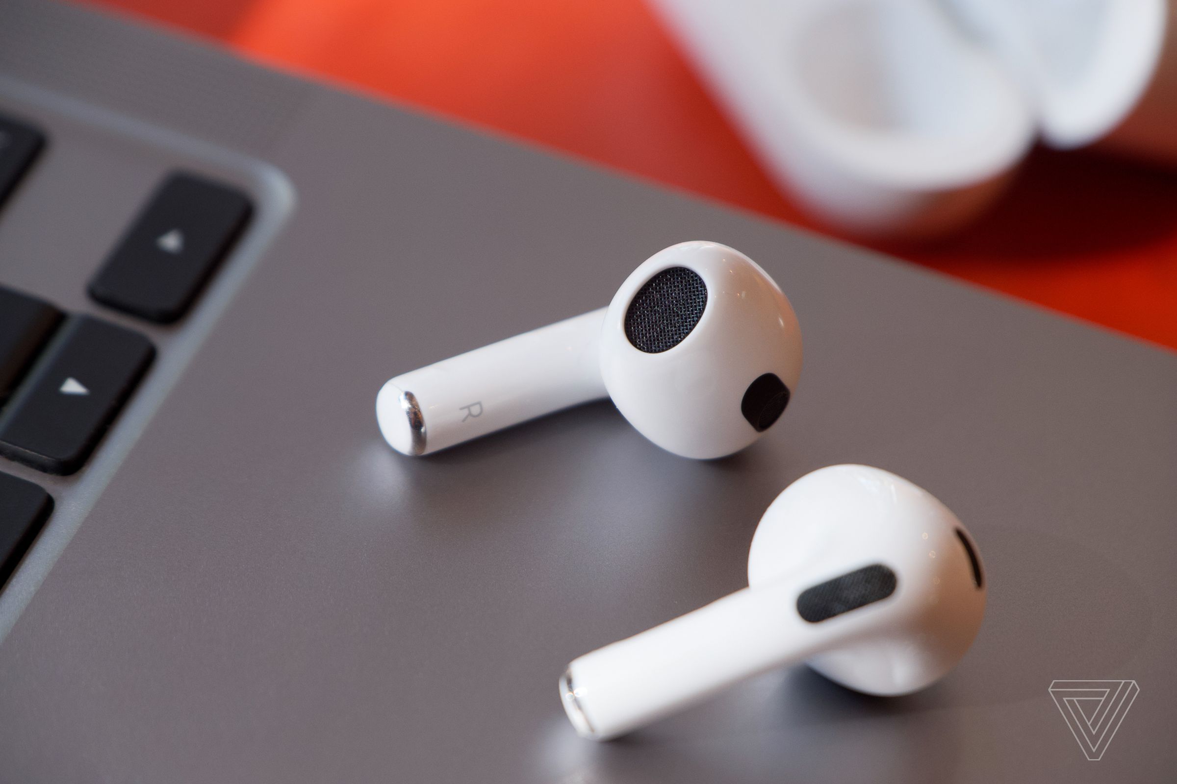 The third-gen AirPods resting on a laptop on a desk.