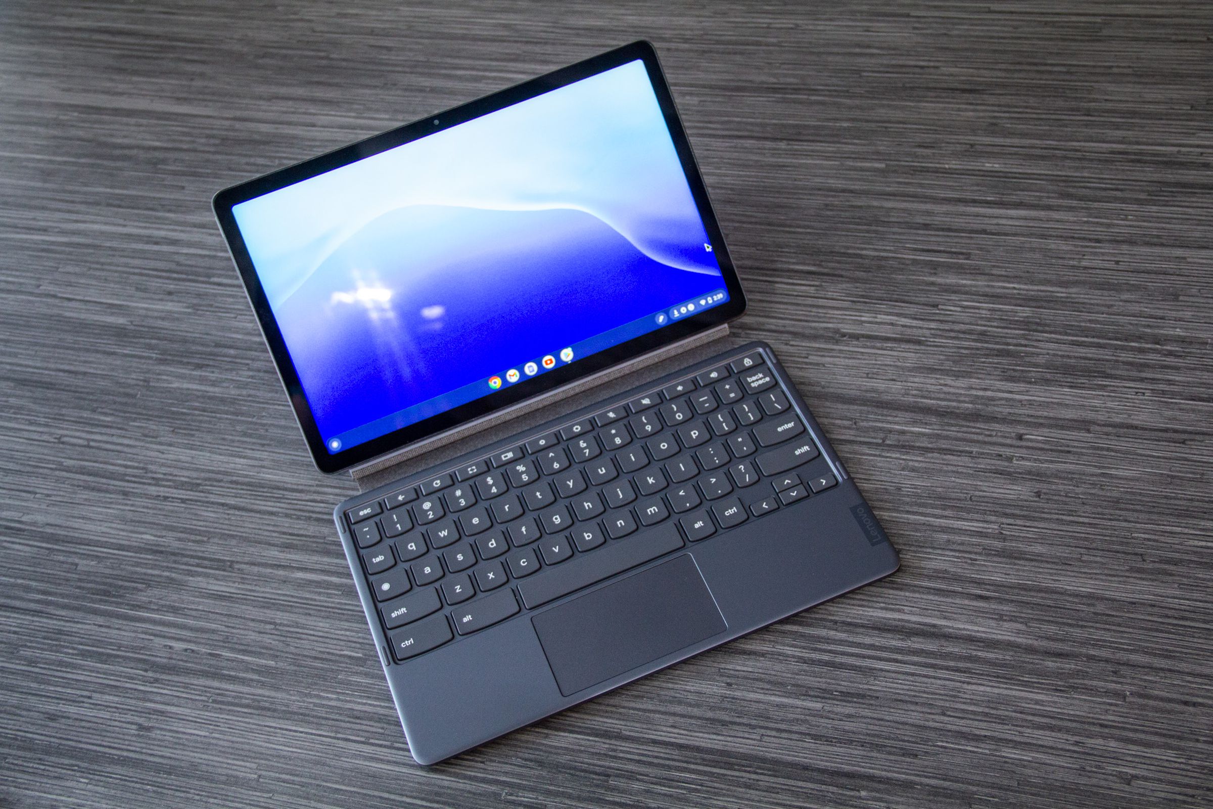 The Lenovo Chromebook Duet 3 in laptop mode on a wooden table seen from above. The screen displays a blue desktop background.