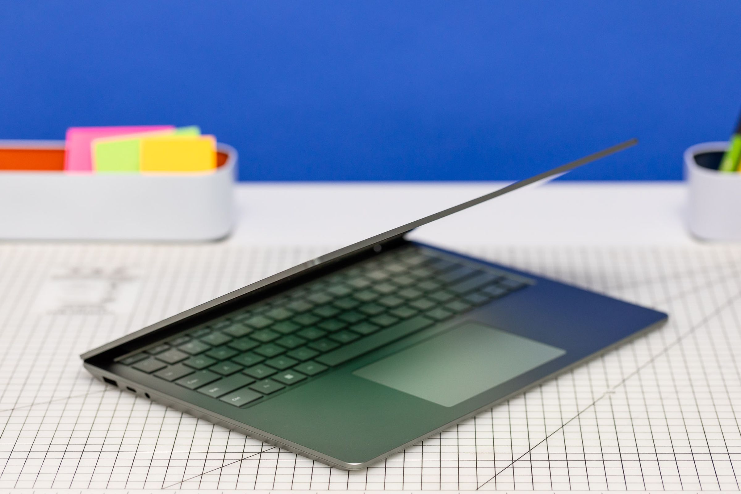 The Surface Laptop 5 half open on a gridded table with post-it notes in the background.