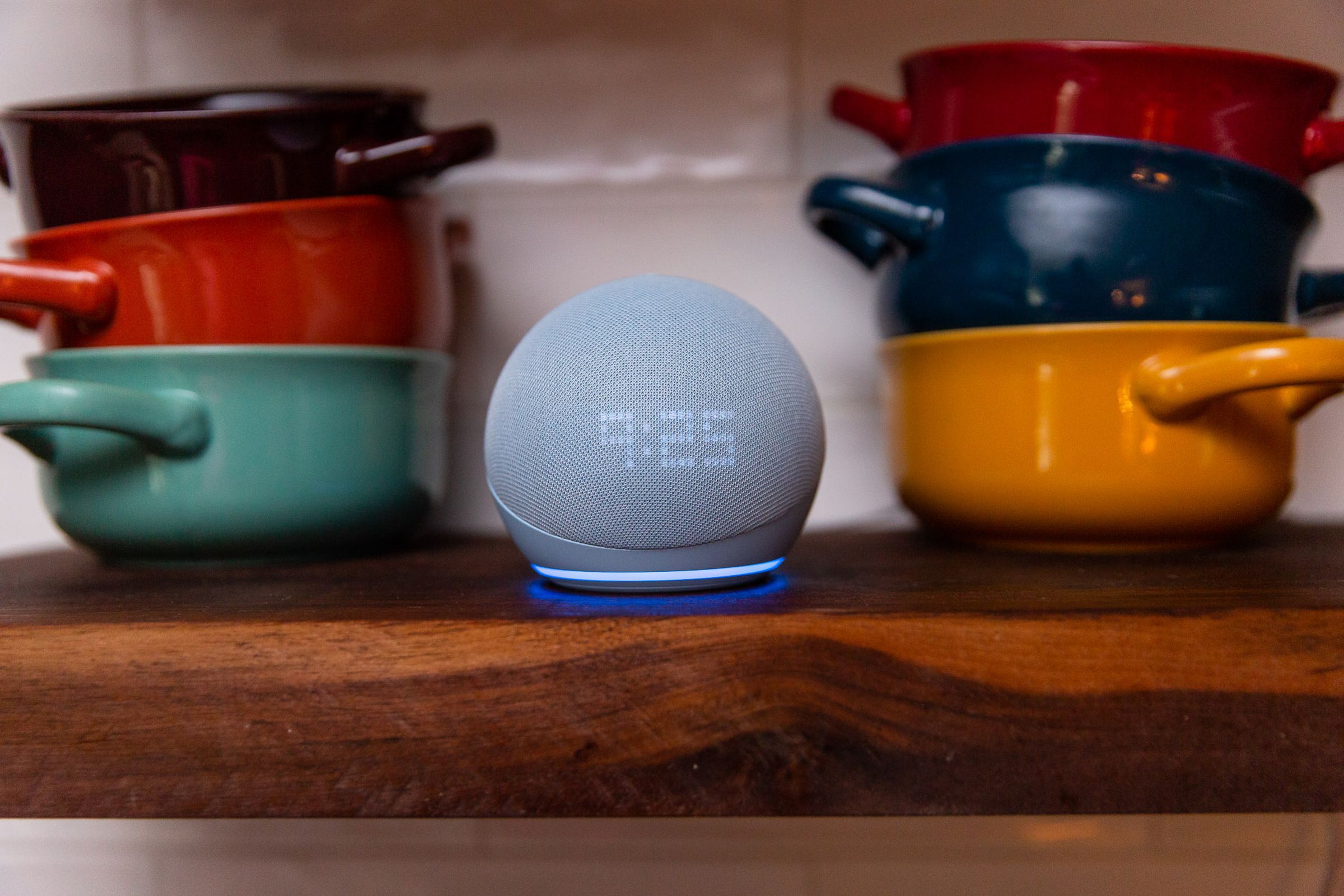 An Echo Dot on a shelf with colorful bowls behind