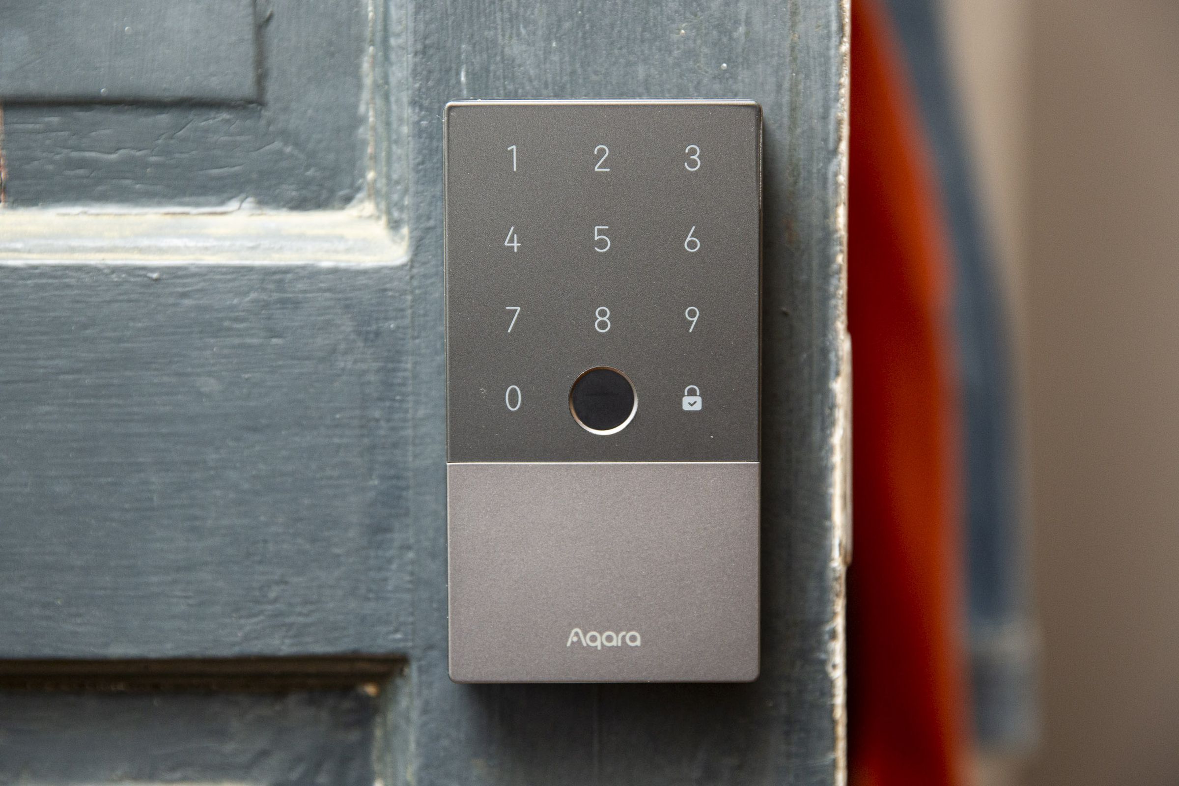 A grey smart lock on a green door that is half open.