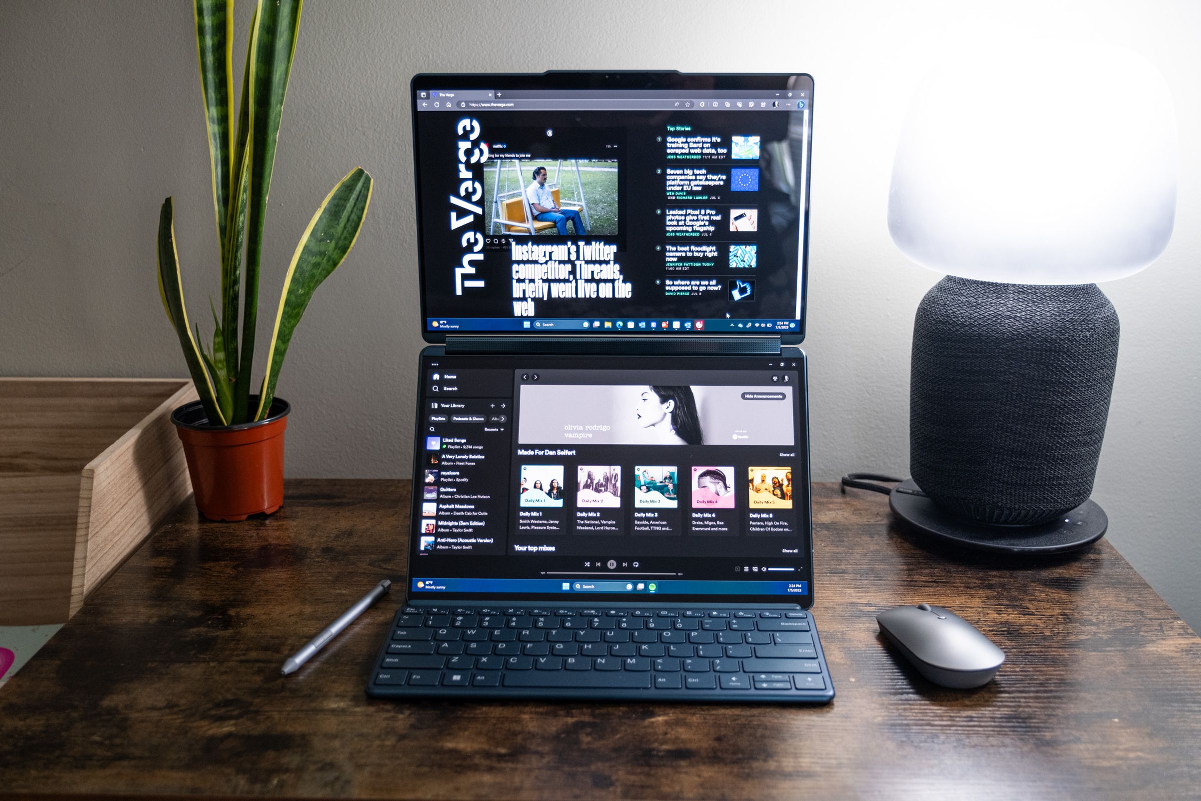 The Yoga Book 9i propped up in dual-screen mode on its included stand and with the Bluetooth keyboard, mouse, and stylus.