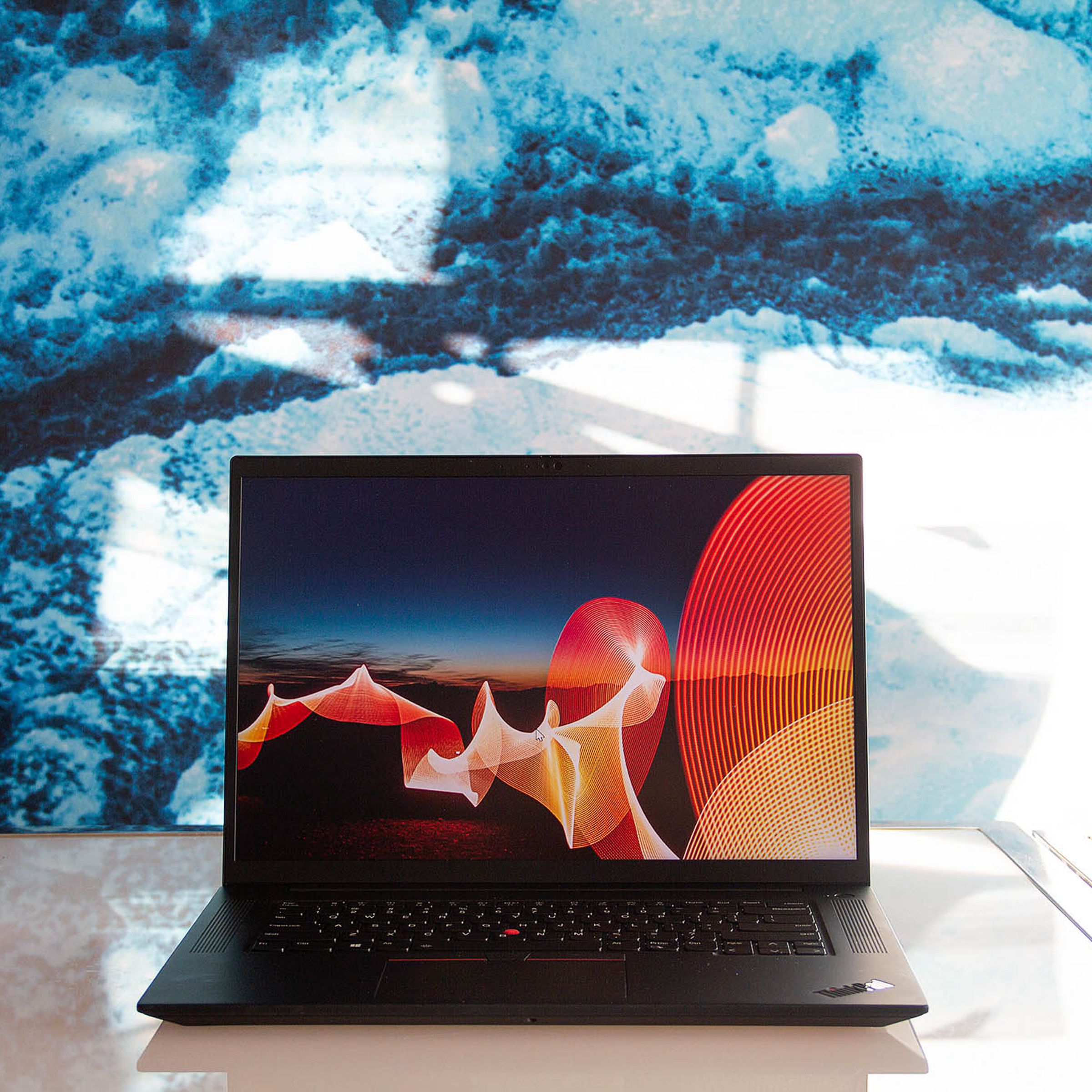 The Lenovo ThinkPad X1 Extreme open on a white table. The screen displays a desert night scene with a bright orange ribbon running through it.