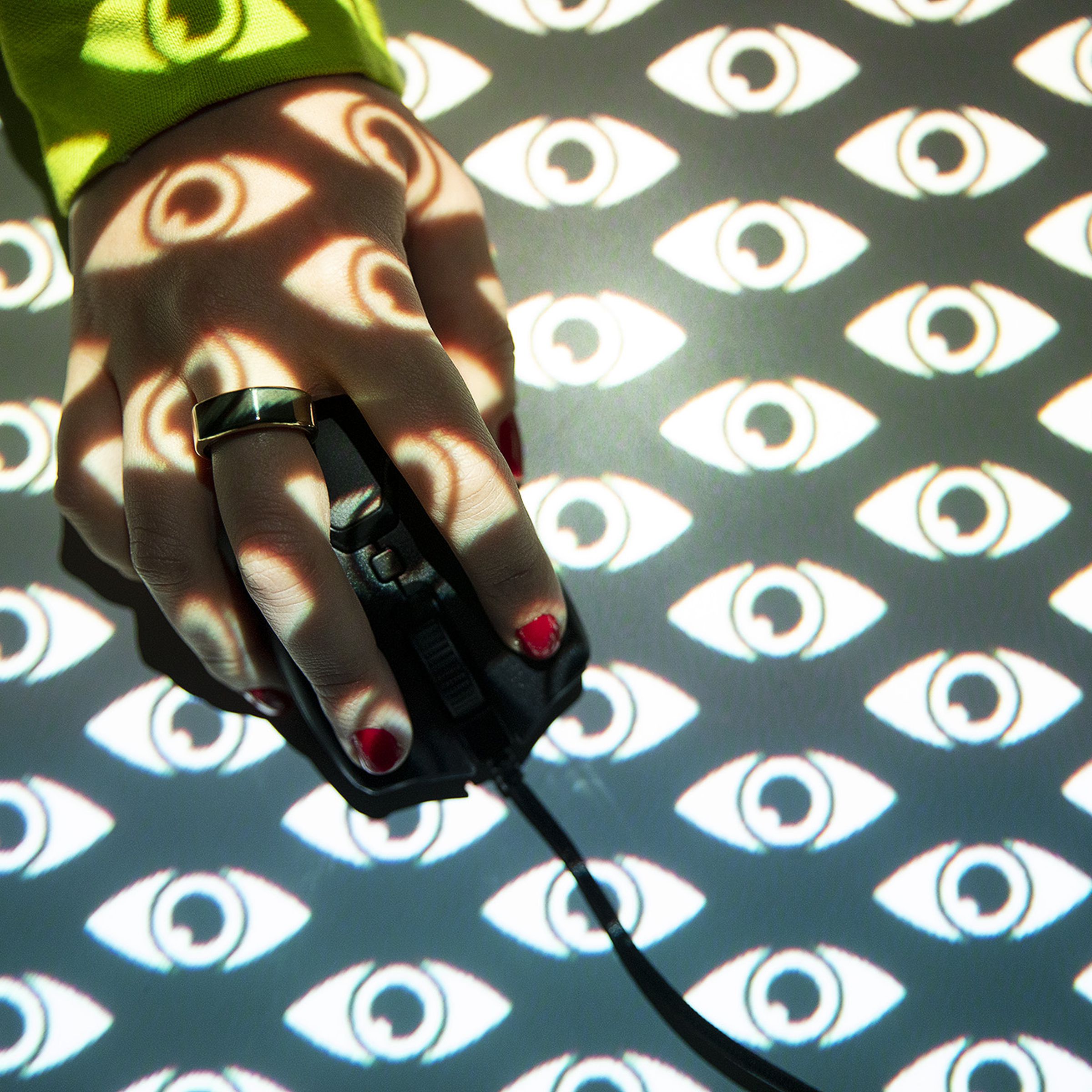 The image shows a hand operating a computer mouse behind an illustrated pattern of eyes.