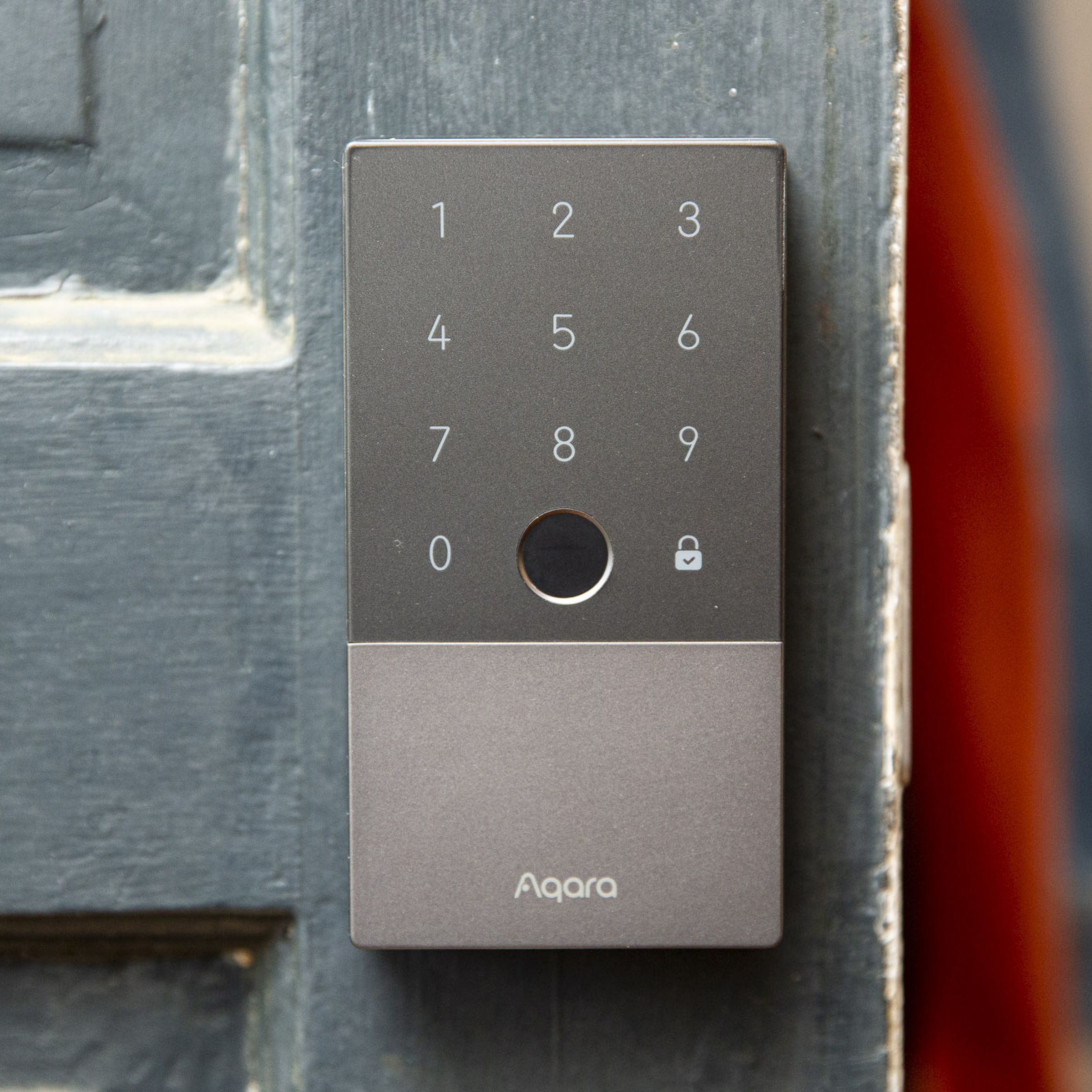 A grey smart lock on a green door that is half open.