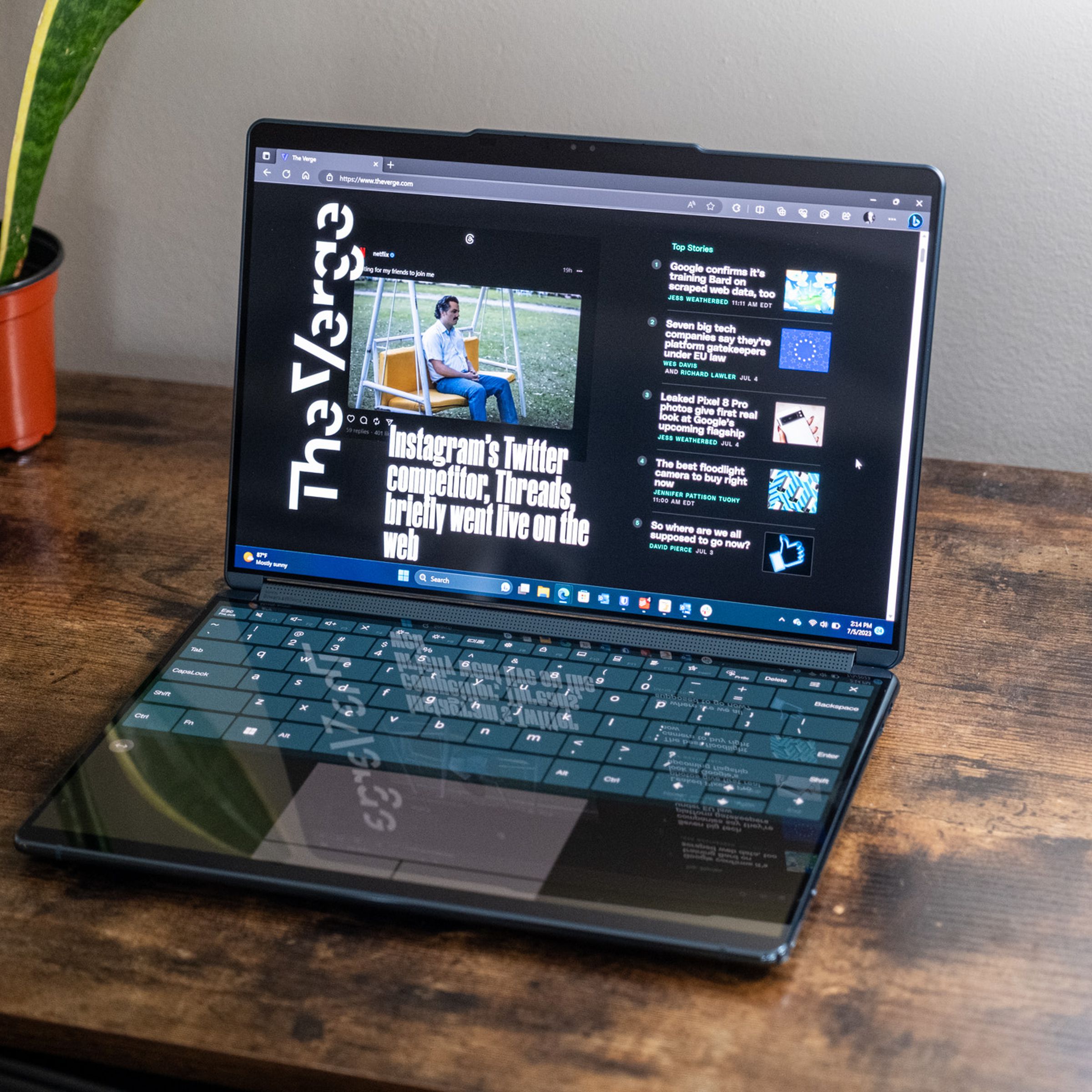 A Lenovo Yoga Book 9i in clamshell mode on a wooden desk.