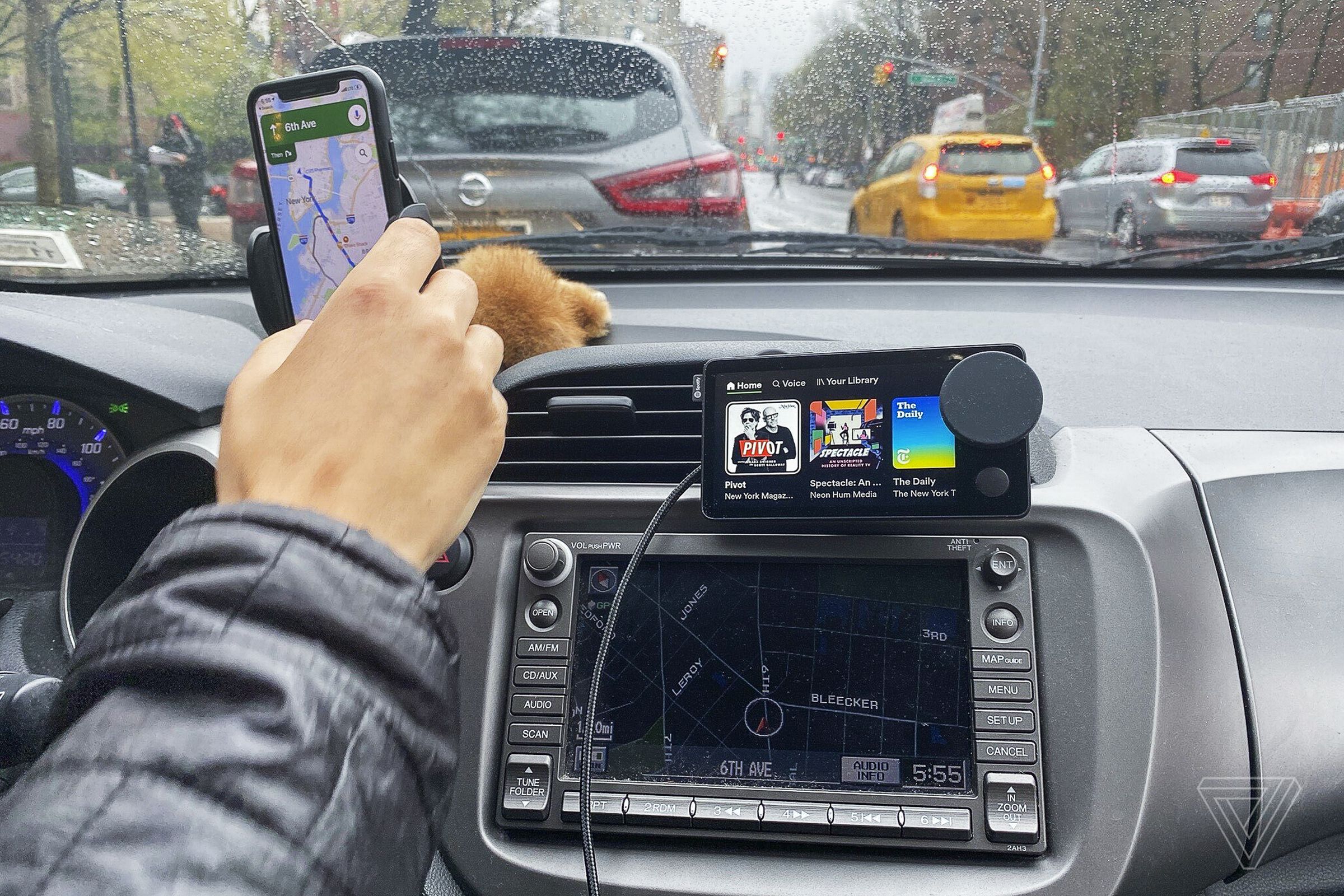 A driver in a car using a Spotify Car Thing and smartphone mounted to the dashboard.