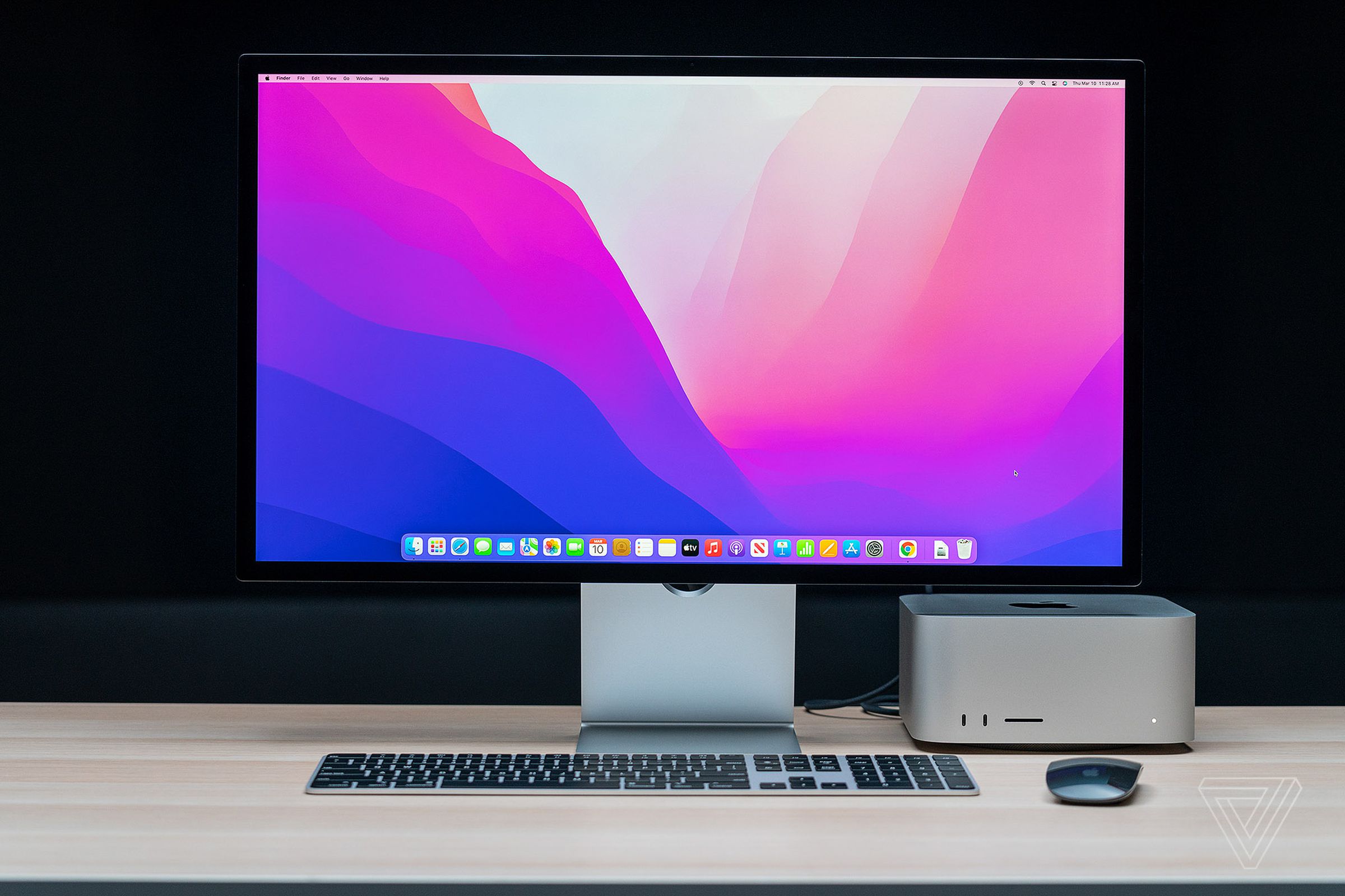 The Mac Studio, Mac Studio Display, keyboard, and mouse seen from the front on a wooden table.