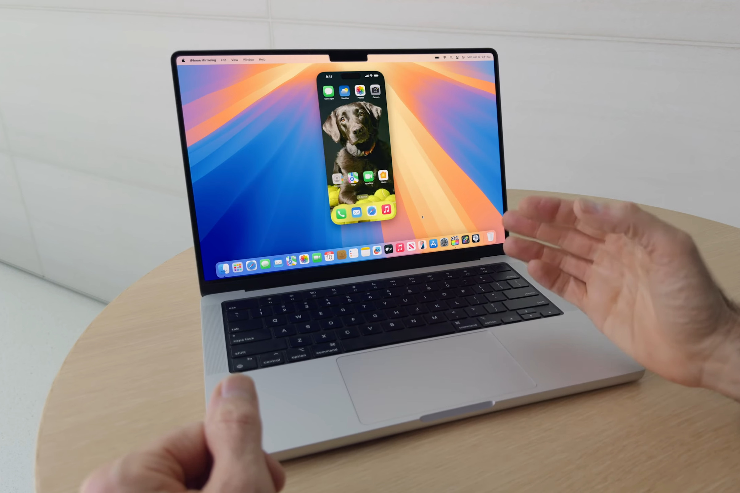 A MacBook Pro on a table shows a mirrored iPhone on its screen.