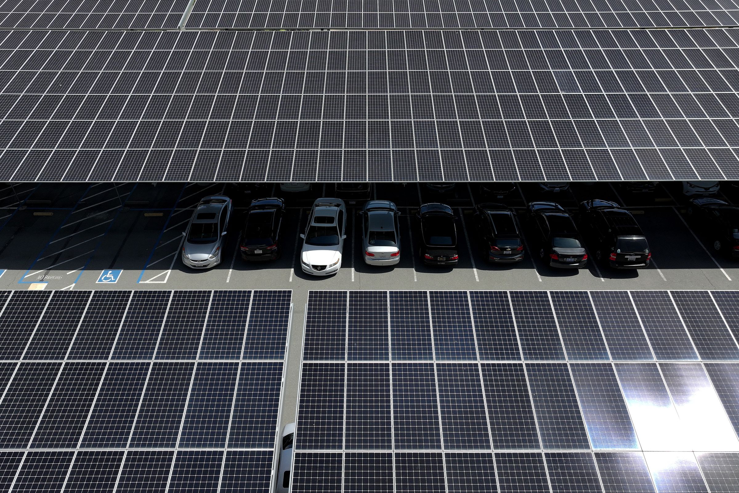 In an aerial view, solar panels are seen in a parking lot shading cars parked underneath them.