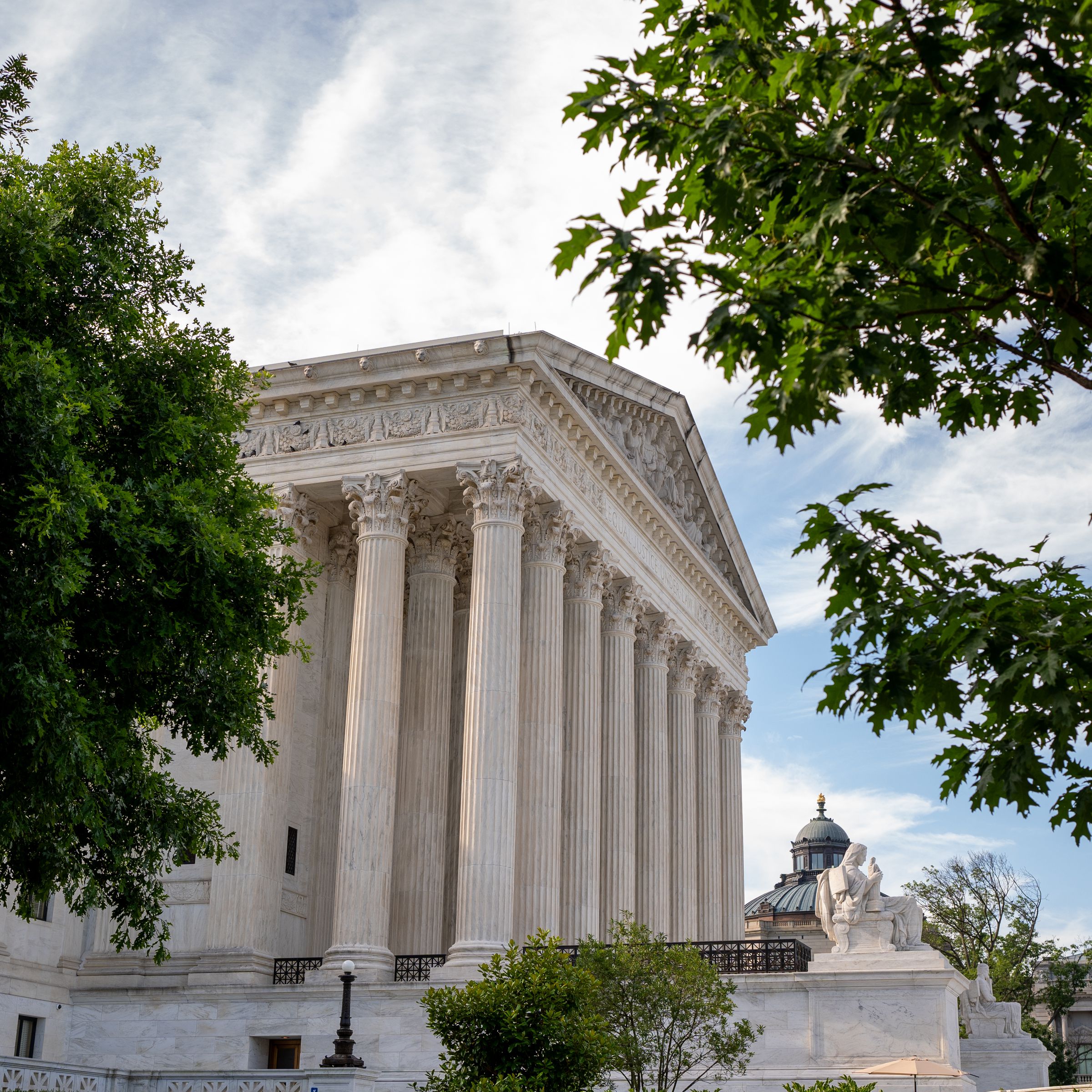 A view of the Supreme Court from the side, partly obstructed by tree foliage.