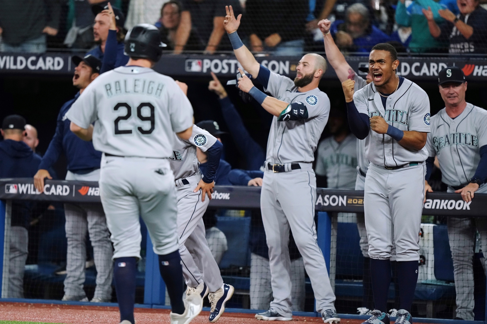 Seattle Mariners Cal Raleigh (29) returns to the dugout after scoring on a double by Adam Frazier against the Toronto Blue Jays during the ninth inning of Game 2 of a baseball AL wild-card playoff series Saturday, Oct. 8, 2022, in Toronto. At right front is Julio Rodriguez / AP.