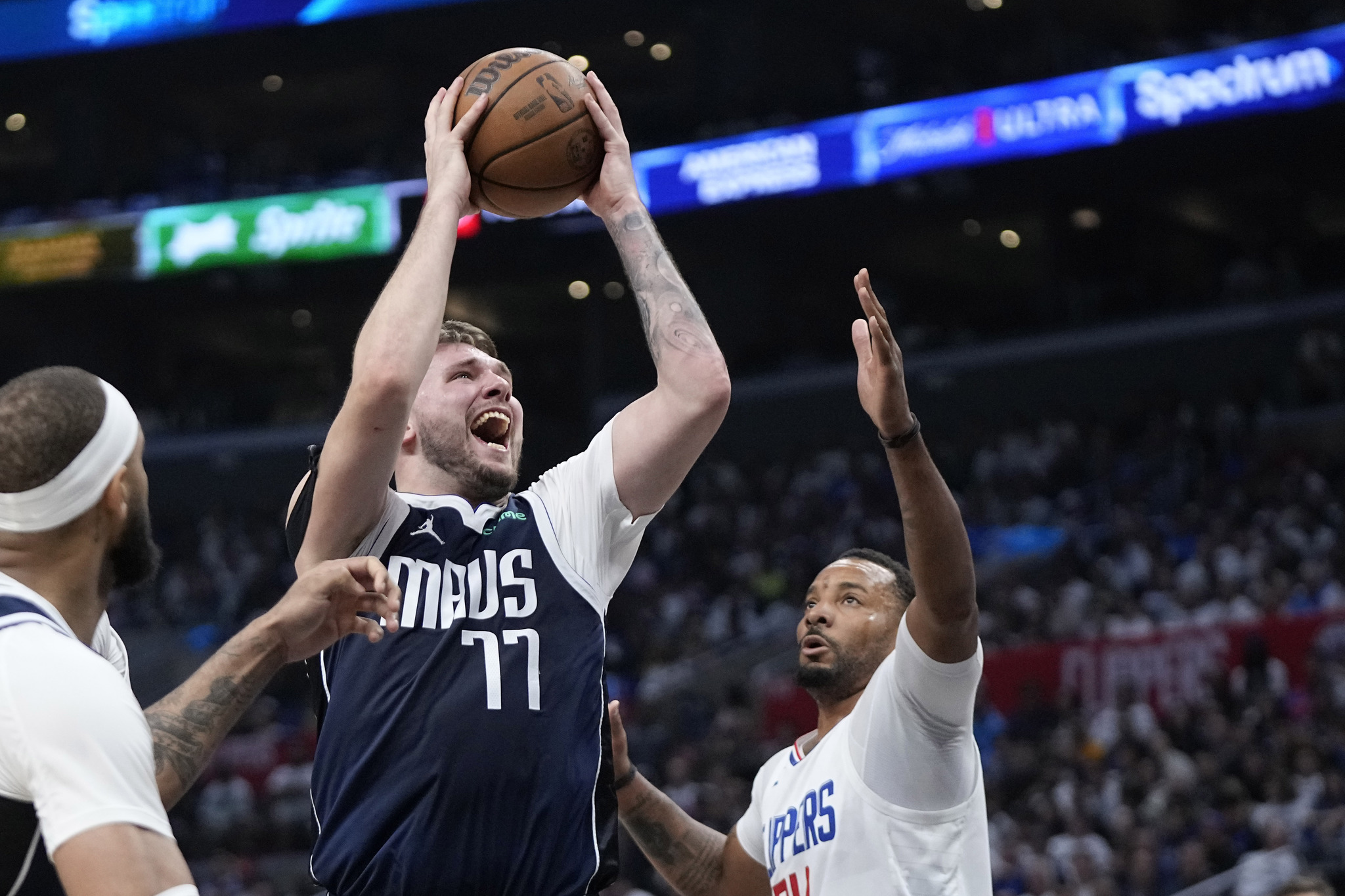 .Dallas Mavericks guard Luka Doncic, center, shoots as Los Angeles Clippers guard Norman Powell, right, defends.