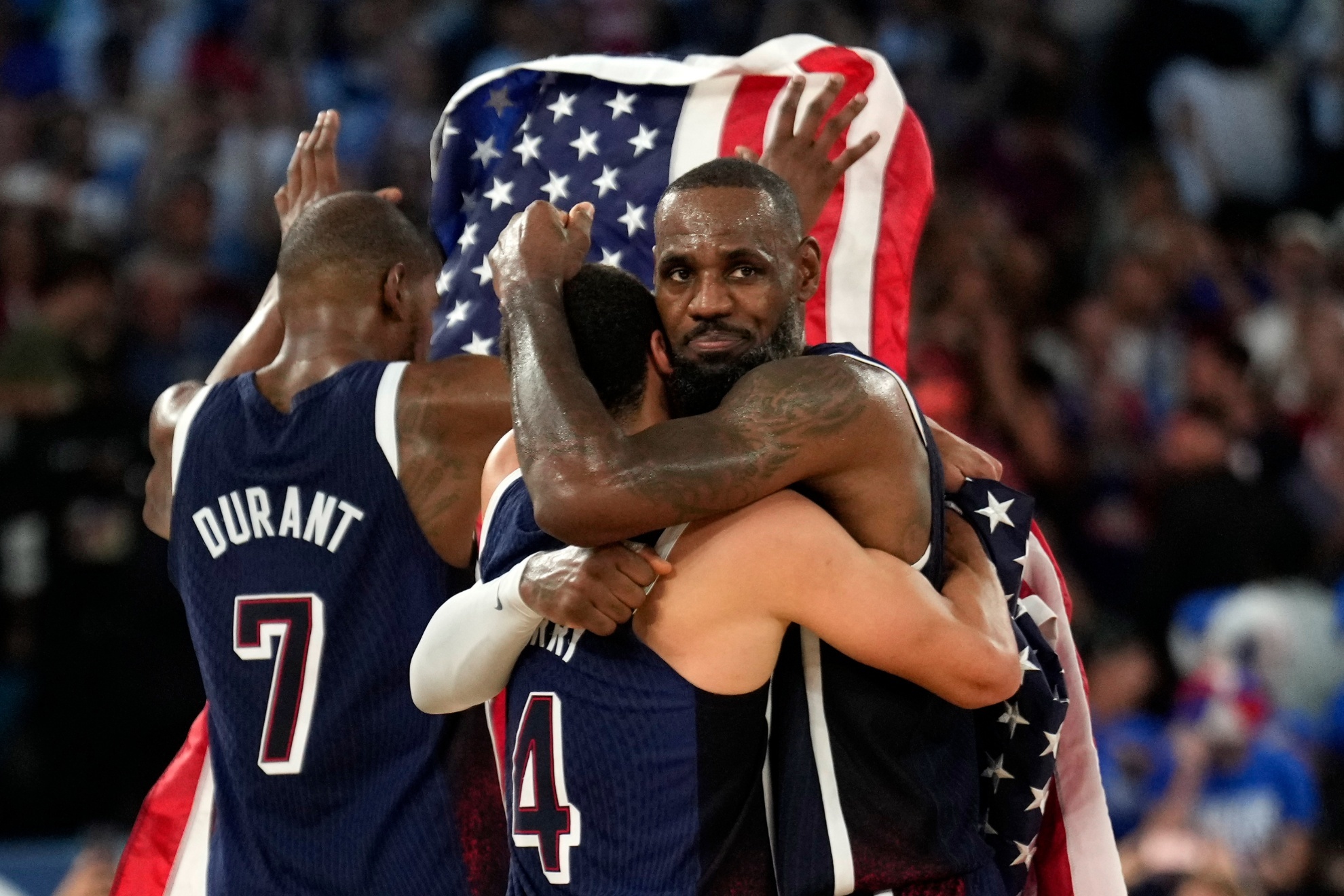 United States Stephen Curry, center, hugs United States LeBron James, right, as United States Kevin Durant hold up an American flag after the United States won a mens gold medal basketball game at Bercy Arena at the 2024 Summer Olympics, Saturday, Aug. 10, 2024, in Paris, France. (AP Photo/Mark J. Terrill)