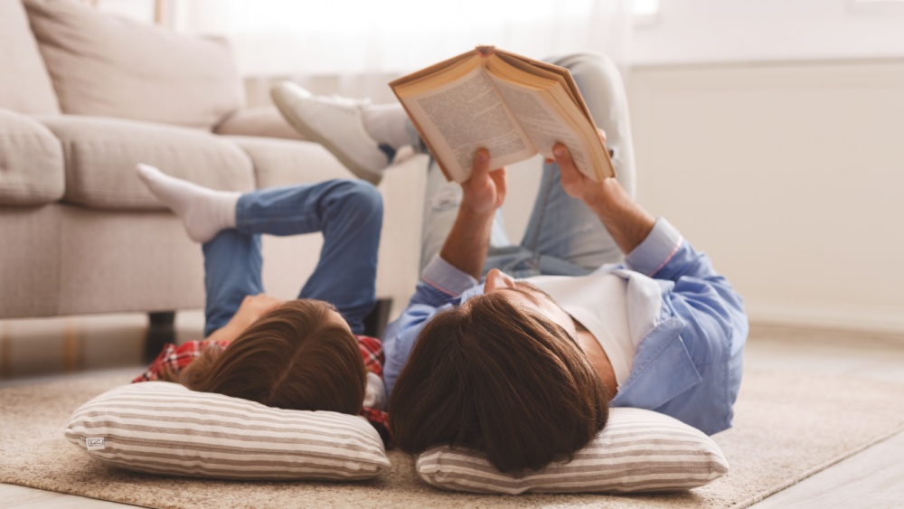 A child and an adult are lying on the floor. The adult is reading a book.