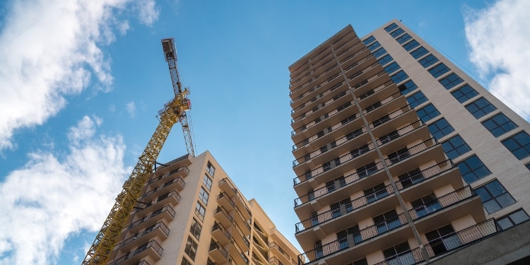 A view looking up at two high-rise apartment buildings and a crane against the backdrop of a blue sky