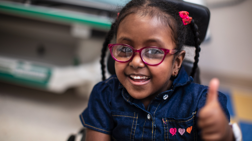 A smiling young girl in wheelchair giving a thumbs up