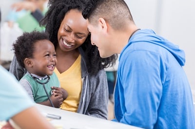 Happy child sits on mother's lap while smiling at health care provider.