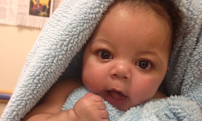 Portrait of baby Nemo, an infant pictured snuggled in a blue blanket.