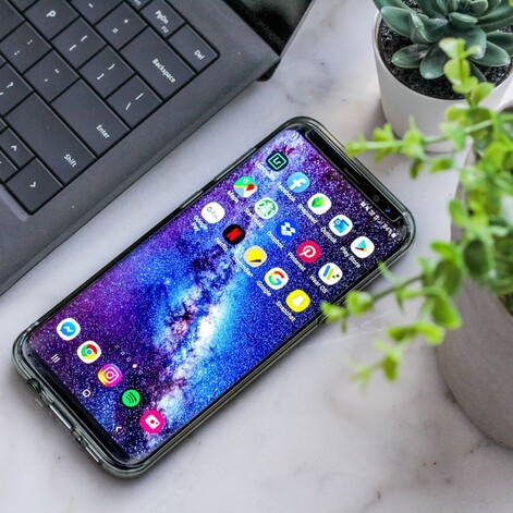 photo: cell phone sitting next to laptop and potted plant