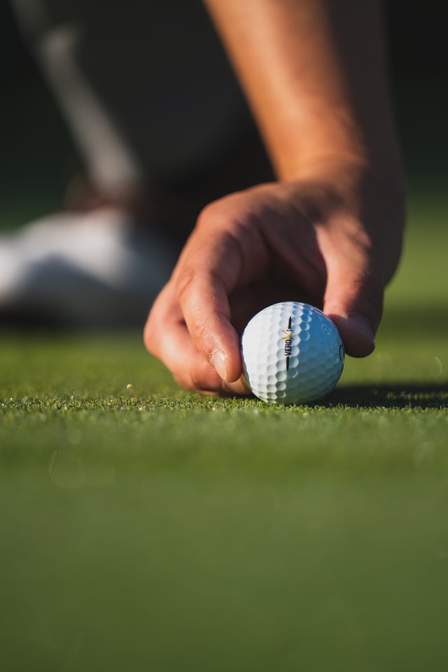 photo: close up of hand placing golf ball on the green