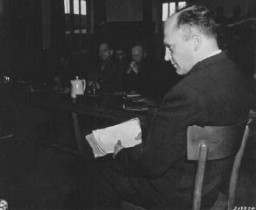 Friedrich Hoffman, holding a stack of death records, testifies about the murder of 324 Catholic priests who were exposed to malaria during Nazi medical experiments at the Dachau concentration camp. Dachau, Germany, November 22, 1945.