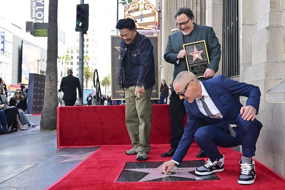 Robert Downey Jr places the first piece of gum on John Favreau's just unveiled Hollywood Walk of Fame Star on February 13, 2023 in Hollywood, California, as Favreau (C) and chef Roy Choi (L) react