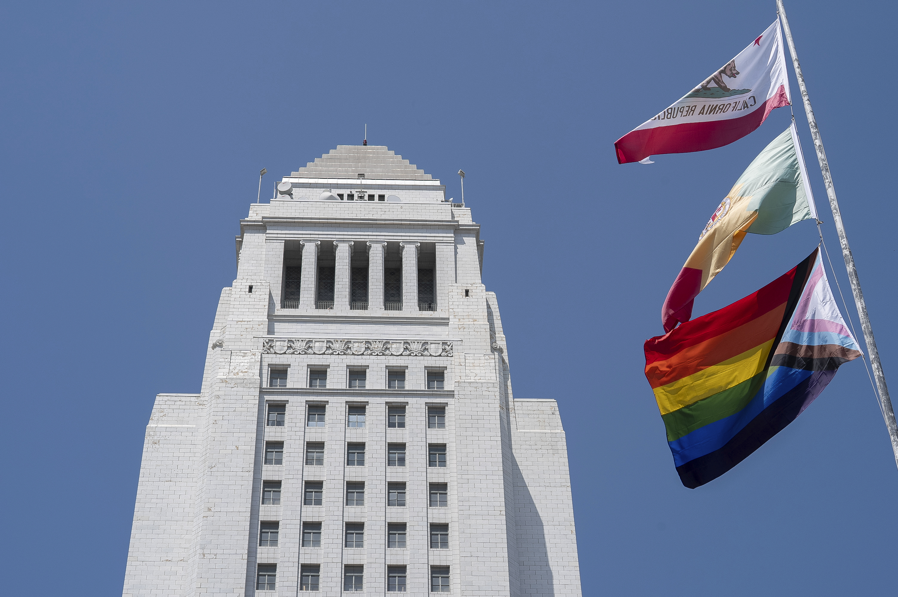 The LGBTQ+ Pride Flag flies with the California State and Los Angeles City flags in Los Angeles