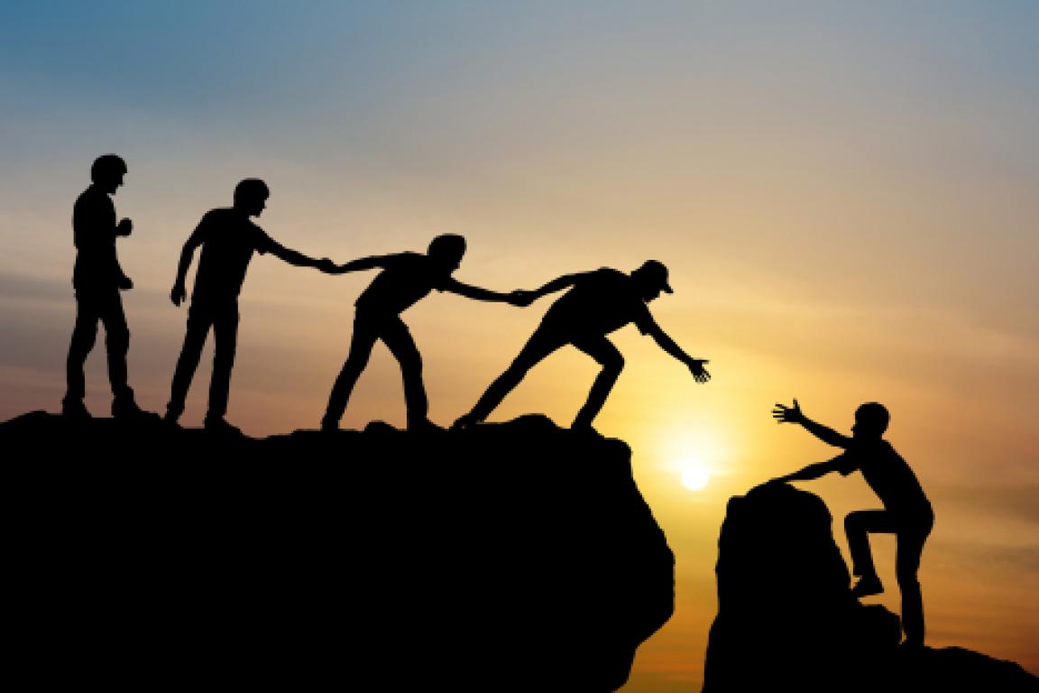 people helping one another climb a rock