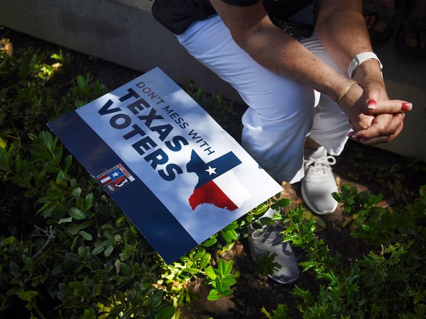 A demonstrator sits beside a sign that reads "Don't Mess With Texas Voters"