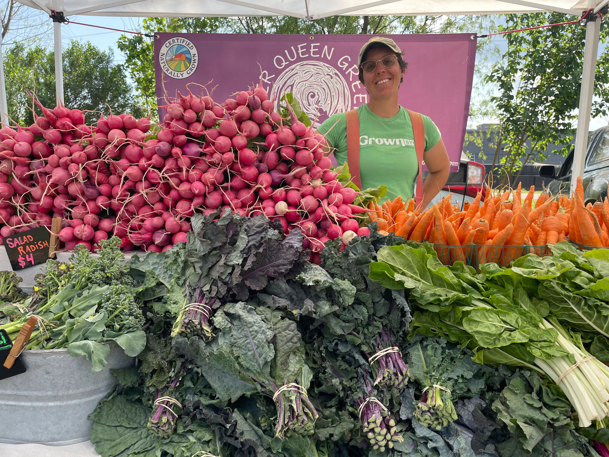 A woman smiling behind fruits and vegetables on a stand