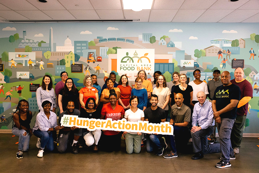 People standing together in front of a HungerActionMonth hashtag with Capital Area Food Bank background