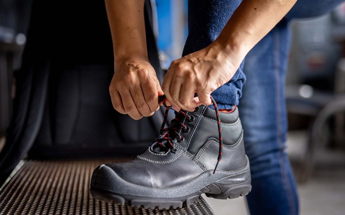 Close-up on a manufacturing worker tying the shoelaces on his work boots at a factory