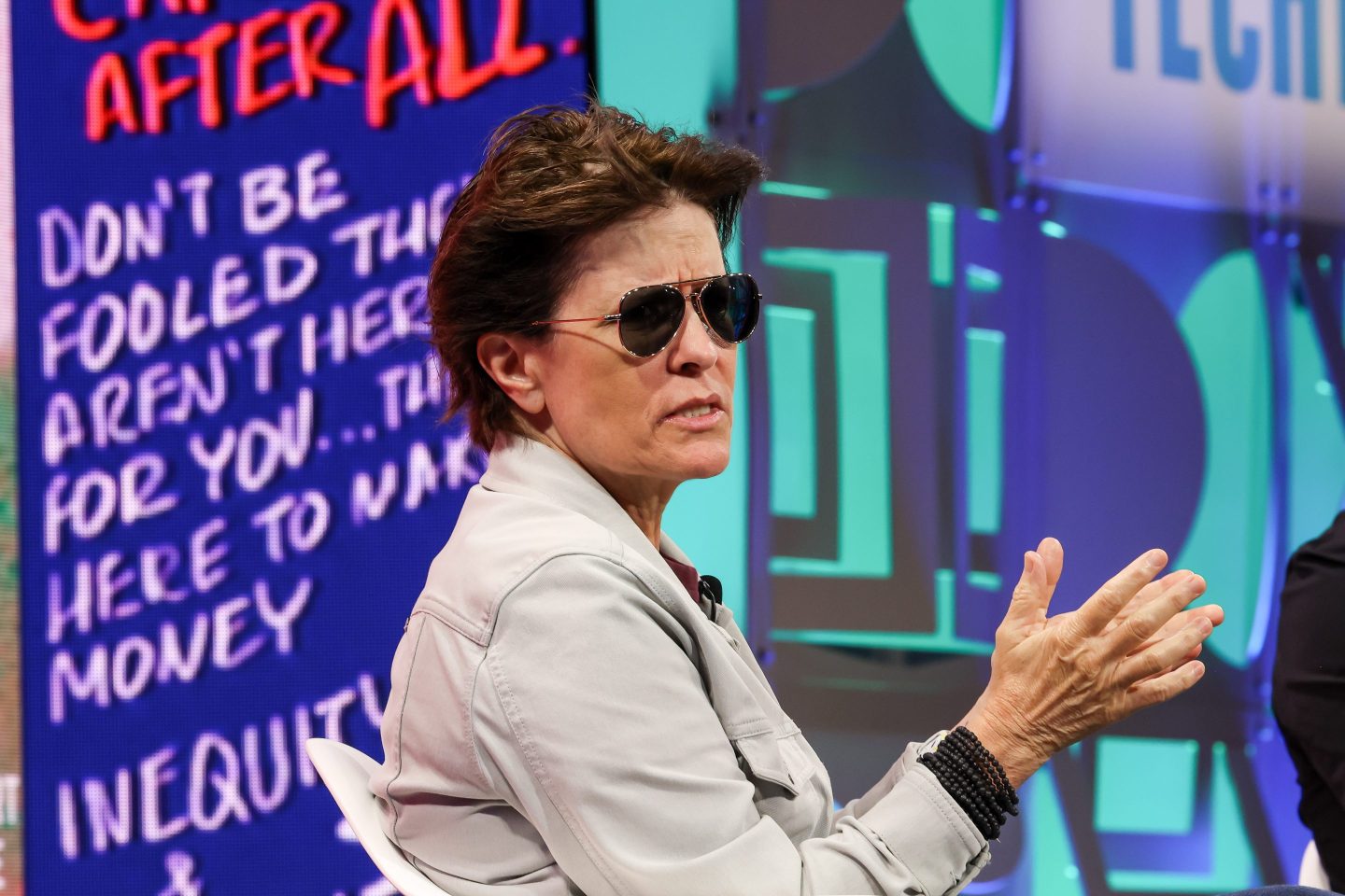 Kara Swisher gestures as she speaks in front of a colorful patterned background.