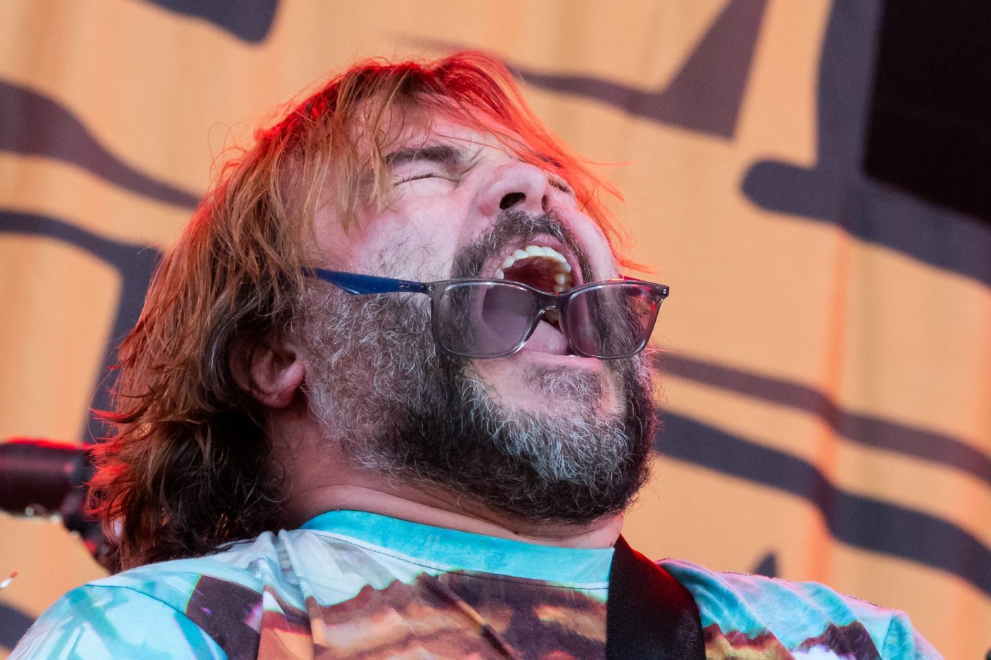 Jack Black letting it rip on stage, with his sunglasses in his mouth