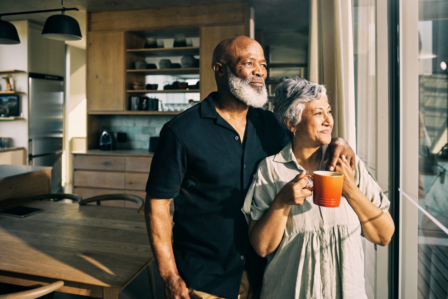 African-American mature couple looking out the window of their home enjoying a moment of togetherness.