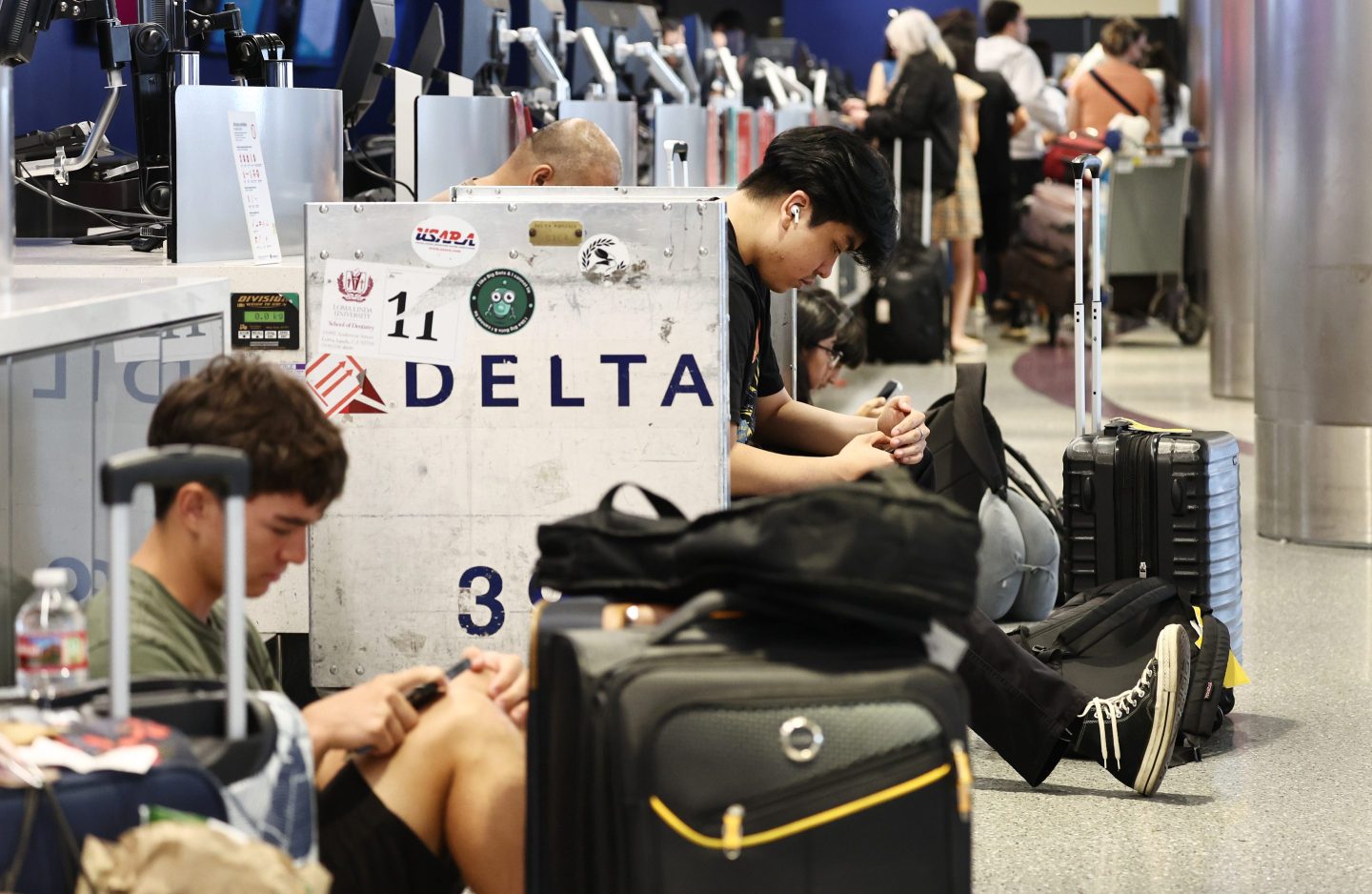 People sit at a Delta terminal with their baggage during this week's chaos.