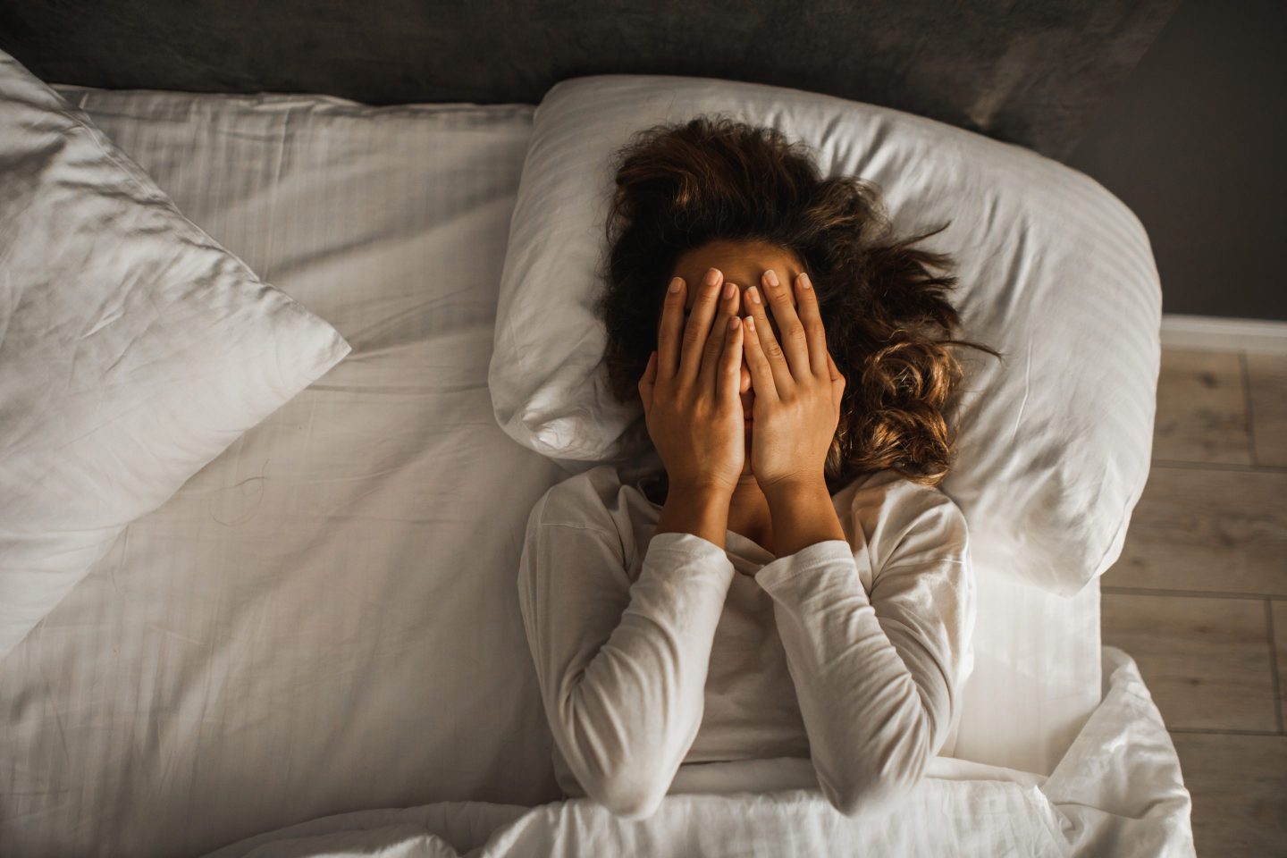 woman lying on her back in bed with her hands over her face