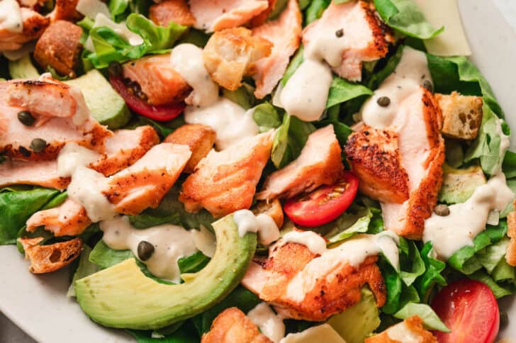 A salad made with lettuce, tomato, avocado, cooked salmon, capers and a homemade caesar dressing recipe.