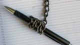 A pen wrapped in an iron chain lies on an empty notebook. Concept- restriction of freedom of speech.