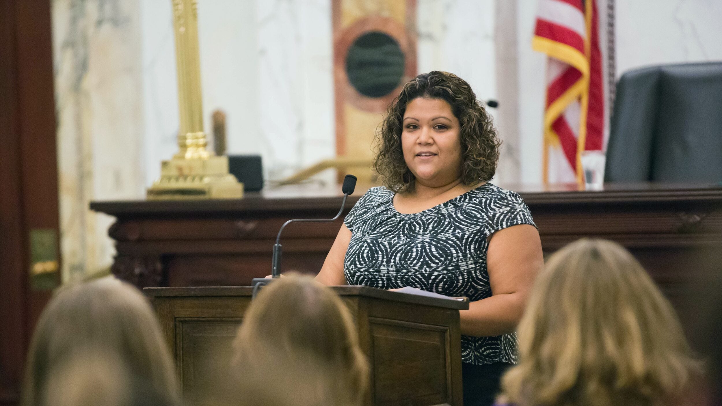 Woman standing at podium talking to group of people.