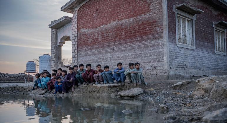 Crianças sentam-se ao lado de um lago de água contaminada da inundação na província de Sindh, no Paquistão.