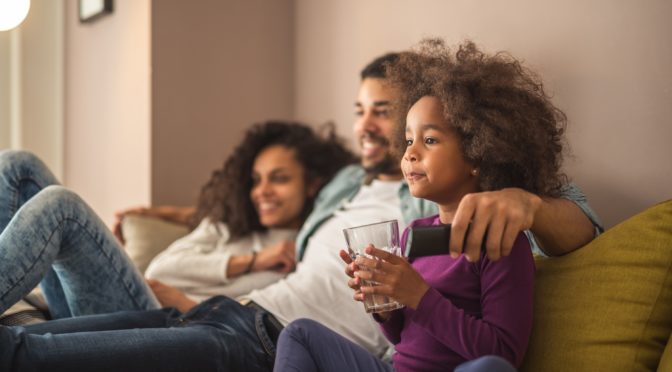 mom, dad and daughter watching TV together on couch