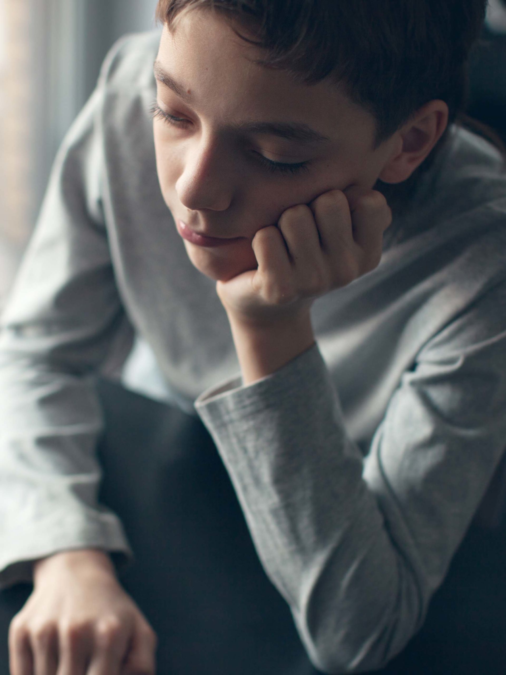 teenage boy rests head on hand and looks moody