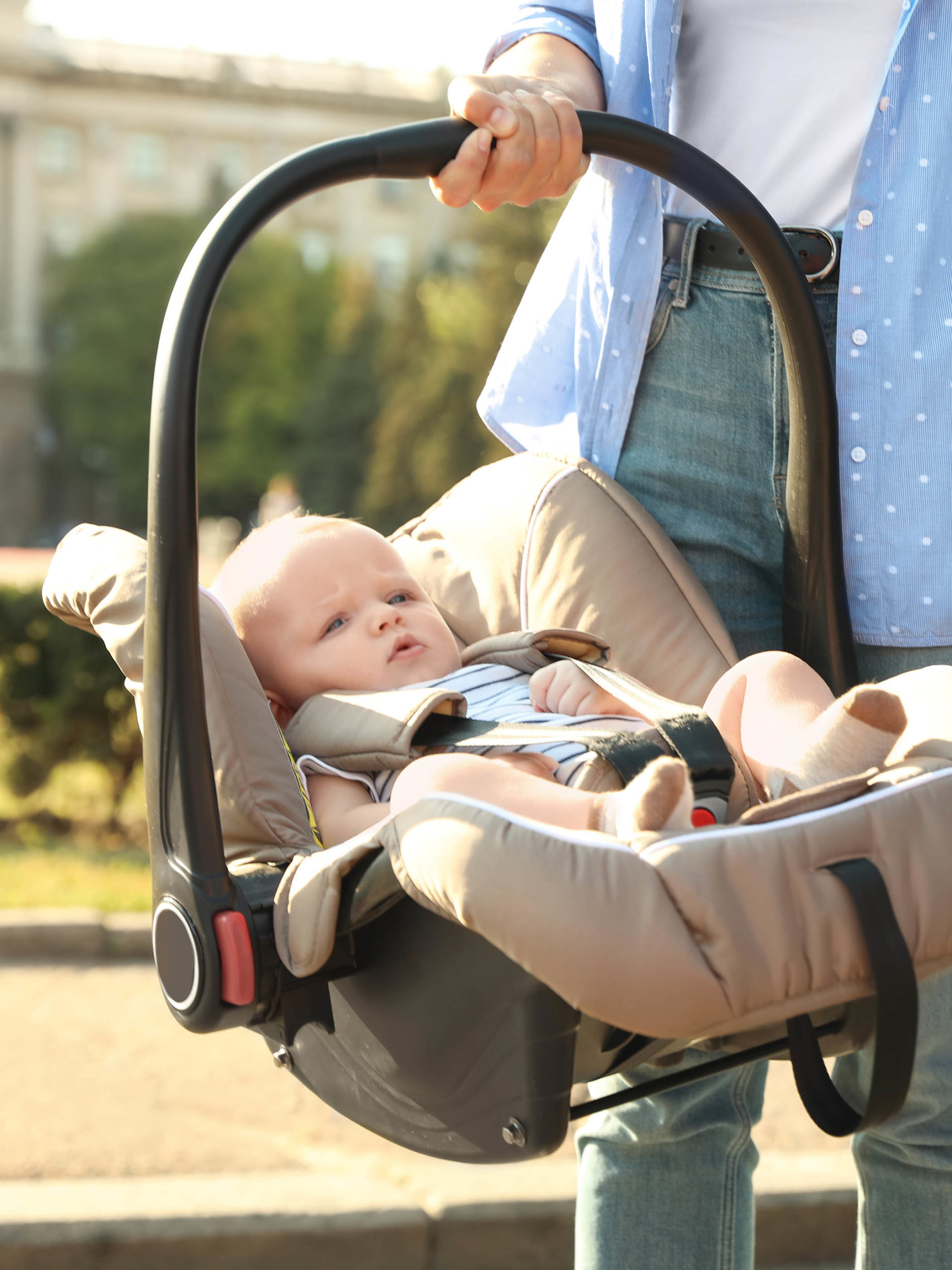 Mother holding child safety seat with baby near car outdoors